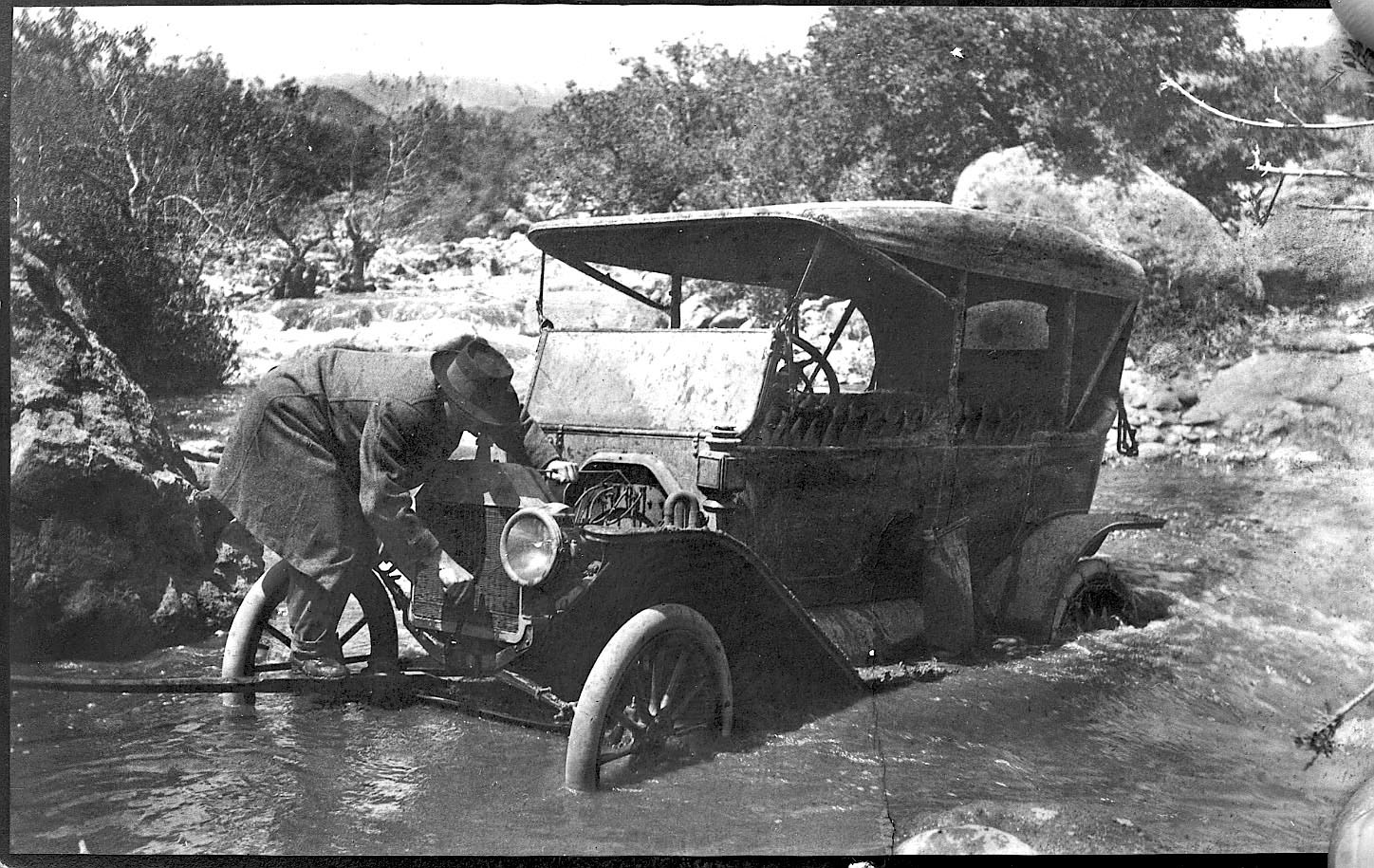 Man trying to get an old car across a stream