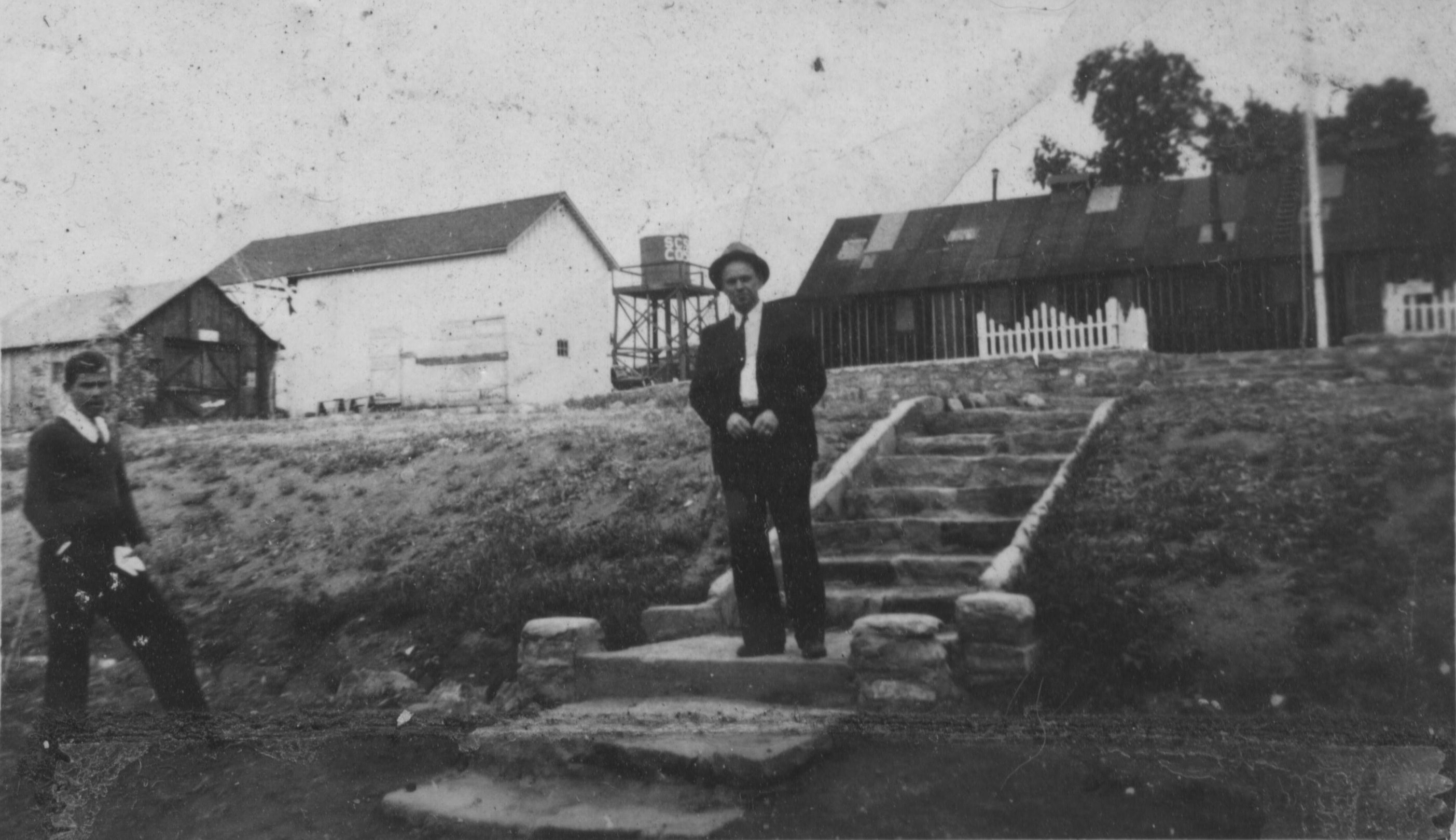 Two men and some of the buildings at the Leeds CCC Camp