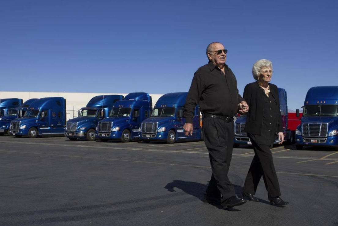 Parke & Emily Cox walking in front of a line of their trucks